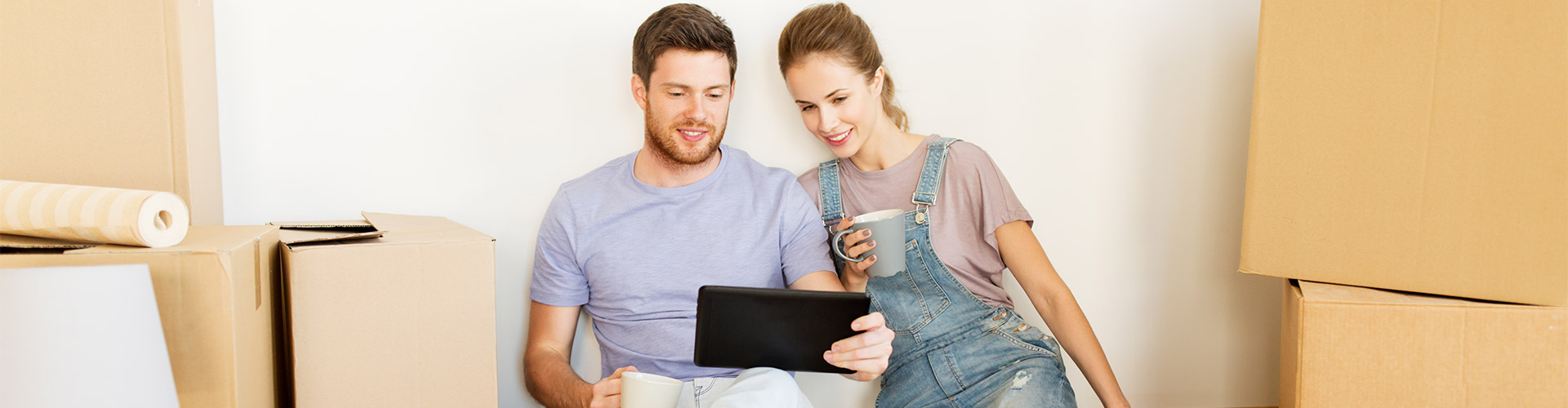 Hipoteca Vivienda - Una pareja sentada en el suelo entre cajas de mudanza con una tableta digital 