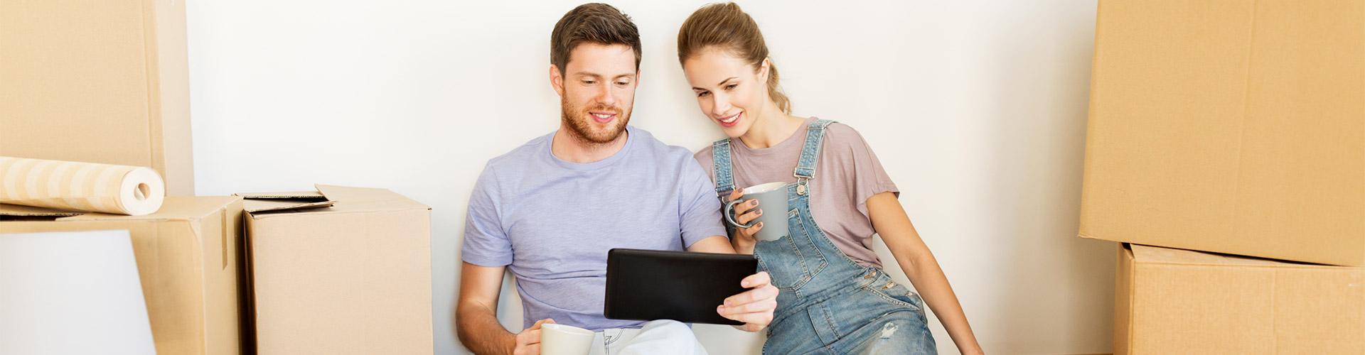 Hipoteca Vivienda - Una pareja sentada en el suelo entre cajas de mudanza con una tableta digital 